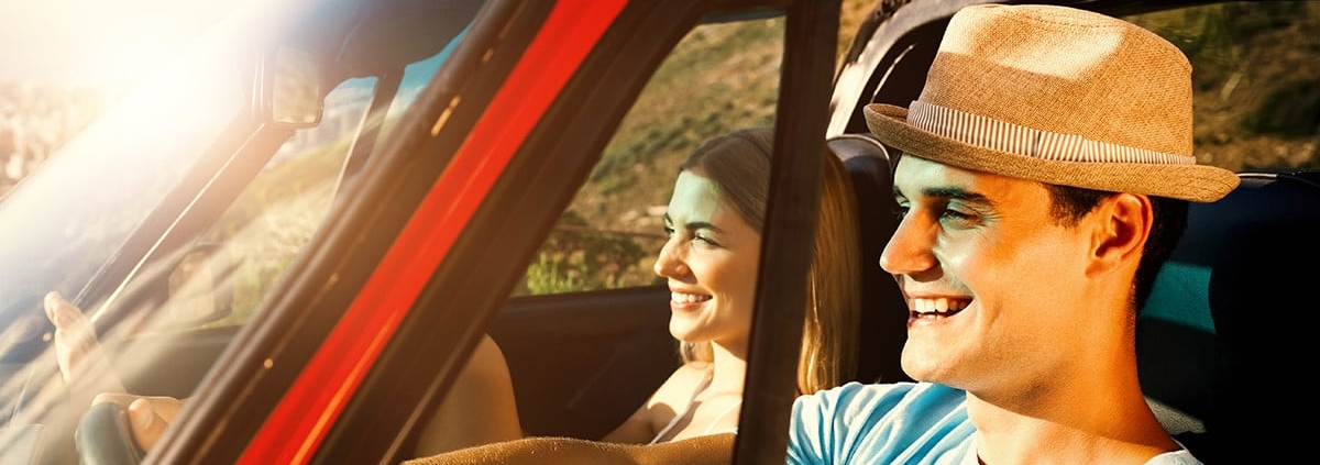A man and woman in a red car smiling under the sunshine.