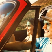 A man and woman in a red car smiling under the sunshine.