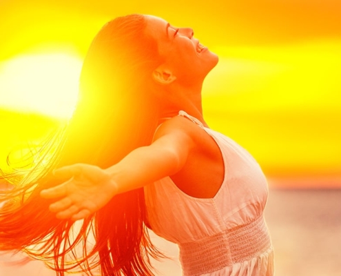 A woman with her arms outstretched at sunset, showcasing a fresh new summer style.