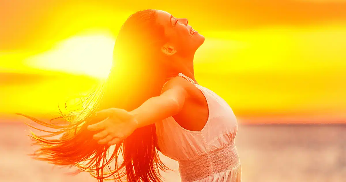 A woman with her arms outstretched at sunset, showcasing a fresh new summer style.