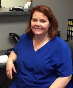 A woman in blue scrubs welcomes new hires at the desk.