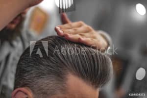 A man with hair loss getting his hair cut in a barber shop.