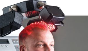 A man with red hair undergoing lower level laser therapy in front of a machine.