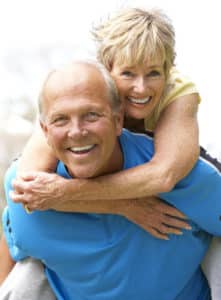 An older couple with thinning hair smiling while carrying each other.