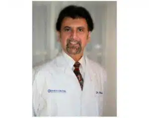A man in a white coat is smiling for the camera while developing a customized treatment plan for hair restoration.