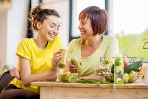 Two women are sitting at a table eating vegetables that promote hormone and thyroid health.