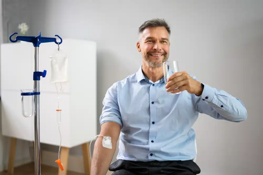 Man Receiving An IV And Drinking Water