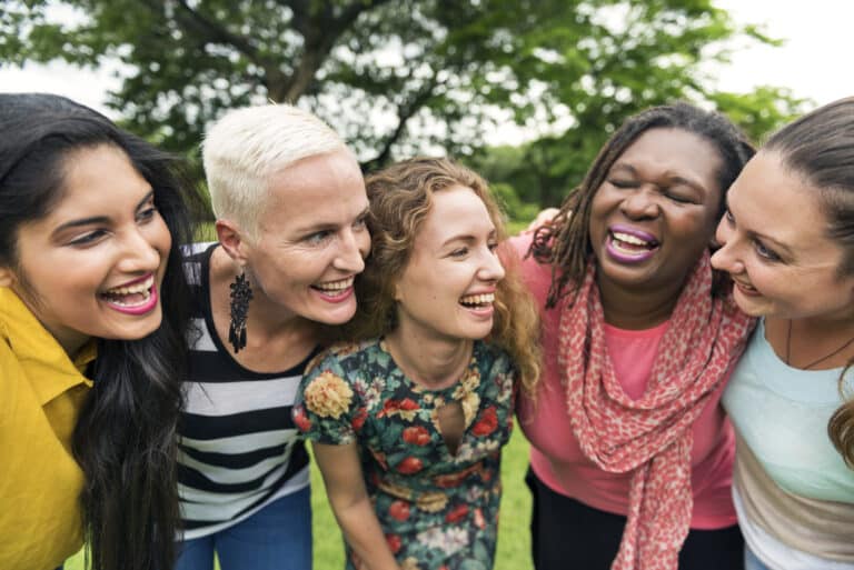 A group of women laughing together in a park, unaffected by hormonal imbalances or hair loss.