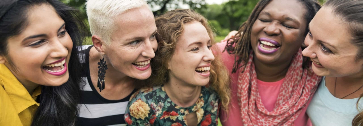 A group of women laughing together in a park, unaffected by hormonal imbalances or hair loss.