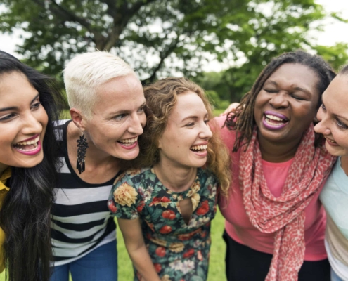 A group of women laughing together in a park, unaffected by hormonal imbalances or hair loss.