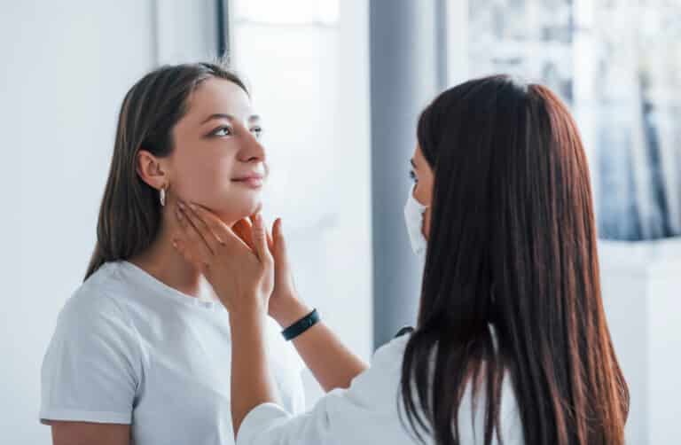 A doctor is examining a woman's neck to assess her thyroid health and investigate possible causes of hair loss.