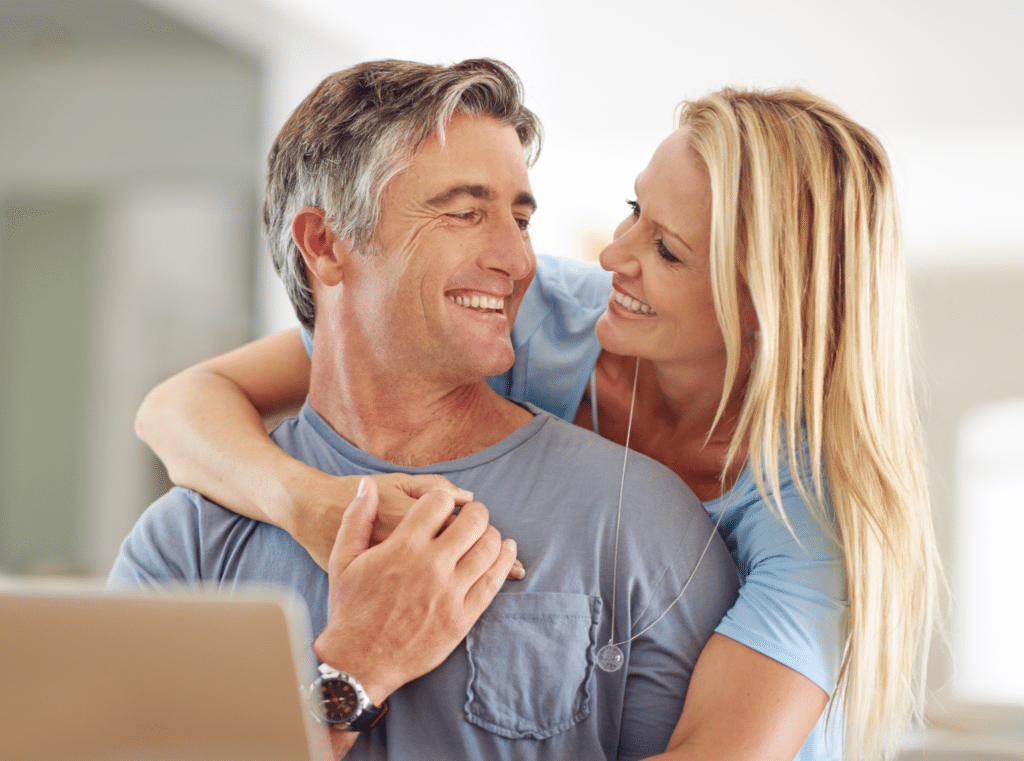 A man and woman happily hugging in front of a laptop.