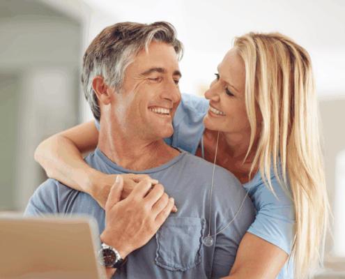 A man and woman happily hugging in front of a laptop.