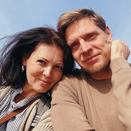 Two people posing for a close-up microneedling selfie outdoors with a clear sky in the background.